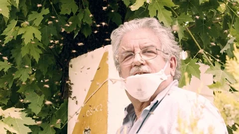 Expert beekeeper smiles at the camera among the flying bees. Stock Footage 155565970
