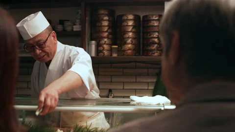 Expert chef prepares dinner for happy Japanese couple sitting at a bar counter g Stock Footage 199455172