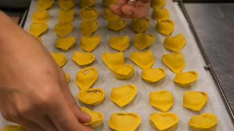 Expert hands arranging fresh handmade tortelli and ravioli pasta on a bakin.. Stock Photos
