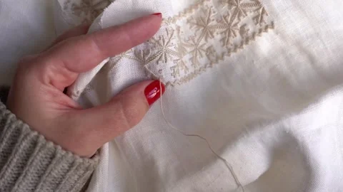 Expert hands create delicate embroidery on a cream fabric with meticulous att Stock Footage 328097563
