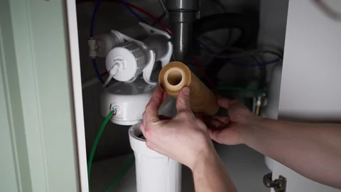 Expert plumber removing a grimy reverse osmosis filter cartridge from under a Stock Footage 326486302