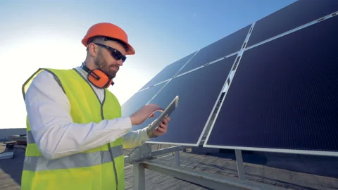 An expert is regulating work of a solar array with his tablet computer. Green Stockbeeldmateriaal 90780466