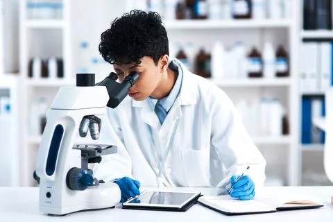 The expert will solve it. a young scientist using a microscope in a lab. Stock Photos