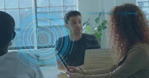 Explaining man in dark tee gesturing in bright office at wooden table with Stock Photos