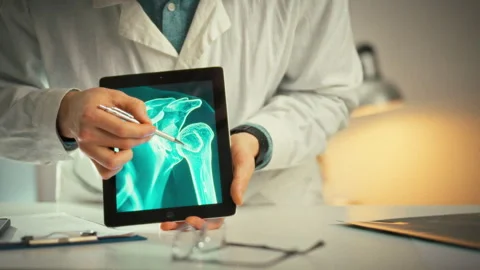 Explaining a shoulder injury a doctor uses a touchscreen tablet in a bright Stock Footage 333501201