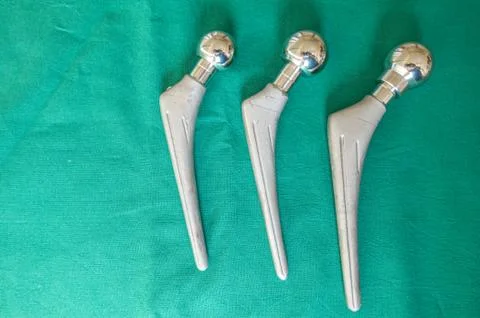 Explanted hip prostheses lie spread out on a green surgical drape Stock Photos