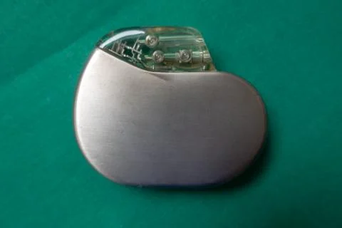 An explanted pacemaker on a green surgical drape Stock Photos