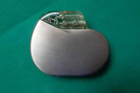 An explanted pacemaker on a green surgical drape Stock Photos