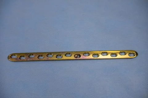 Explanted surgical gold-colored titanium plate lies on an operating table Stock Photos
