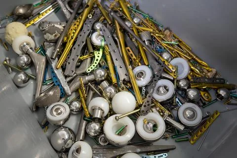 Explanted titanium plates, screws and hip prostheses lie in a gray plastic bo Stock Photos