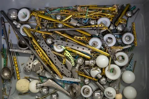 Explanted titanium plates, screws and hip prostheses lie in a gray plastic bo Stock Photos