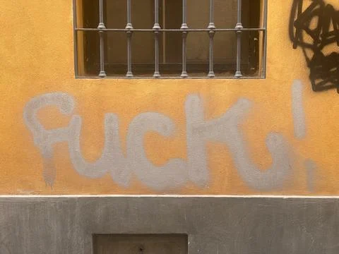 Explicit graffiti text on yellow urban wall with window bars in Cremona, It.. Stock Photos