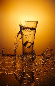 Exploding Glass cup with water shattering over orange background. 写真素材