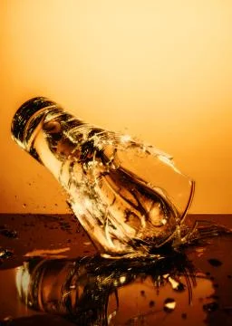 Exploding Glass cup with water shattering over orange background. 写真素材