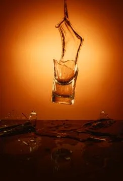 Exploding Glass cup with water shattering over orange background. 写真素材