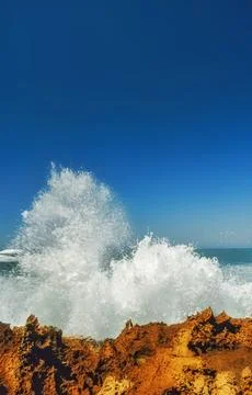 Exploding ocean wave meets rugged rocks beneath deep blue sky Stock Photos