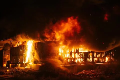 Exploding warehouse. Burning industrial building. Big blaze at night Stock Photos
