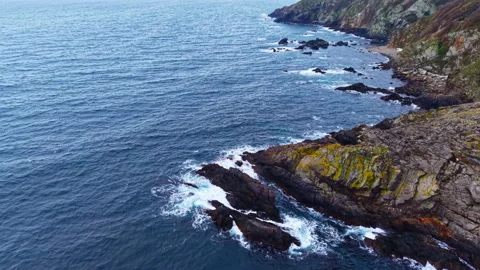 Explore the rugged coastline at dawn where waves crash against dark rocks amidst Stock Footage 321754769