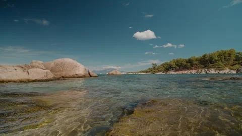 Explore serene turquoise waters and rocky coastline under bright clouds Stock Footage 303513816