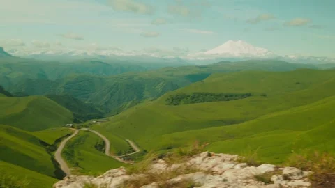 Explore stunning green hills under a clear blue sky with majestic snow-capped Stock-Footage 312516579