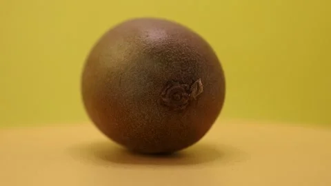 Explore the unique texture and shape of a kiwifruit resting on a vibrant yellow  Stock Footage 328635135