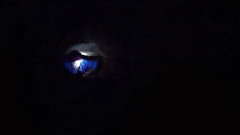 Explorer climbs outward from narrow hole inside cave with flashlight in his hand Stock Footage 80063337