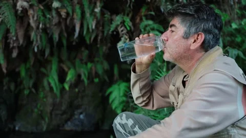 Explorer collecting water from a jungle spring and drinking it to quench his Stock Footage 336688818