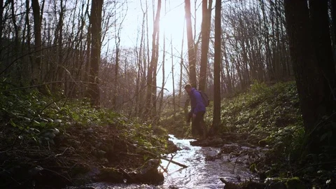 Explorer jumping over a narrow stream in the forest on a sunny day Stock Footage 81536531