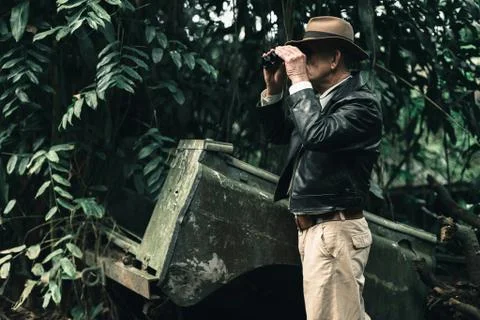Explorer looking with binoculars standing in bush next to car wreckage. Stock Photos