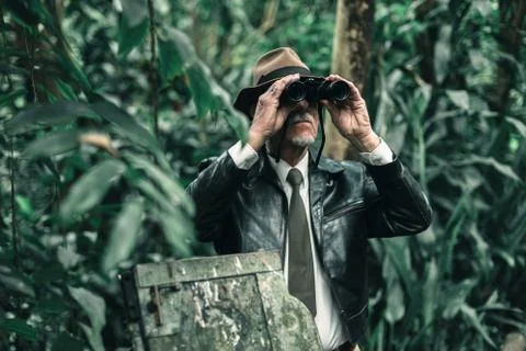 Explorer looking with binoculars standing in bush next to car wreckage. Stock Photos