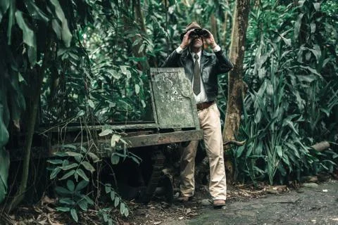 Explorer looking with binoculars standing in bush next to car wreckage. Stock Photos