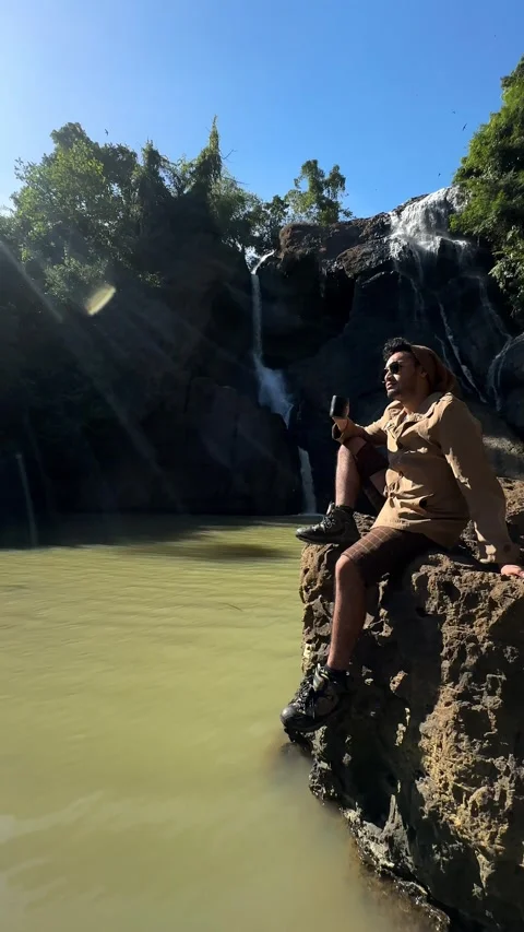 Explorer Man Sitting on Rock, Jungle Waterfall, Vertical Tracking Shot Stock Footage 325646380