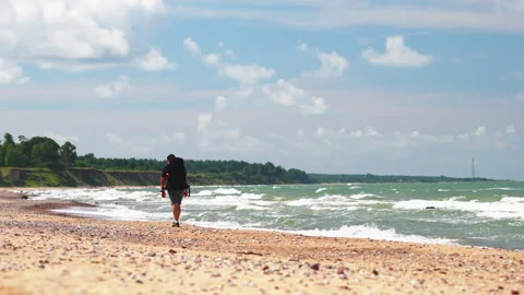 Explorer moving steadily across beach with backpack and surf gear Stock Footage 324918012