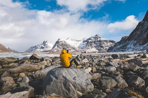 Explorer in a yellow jacket sits on a large rock at Skagsanden Beach, takin.. Stock Photos