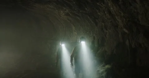Explorers in cave hiking past camera with headlamps shinning through smoke Stock Footage 64685160