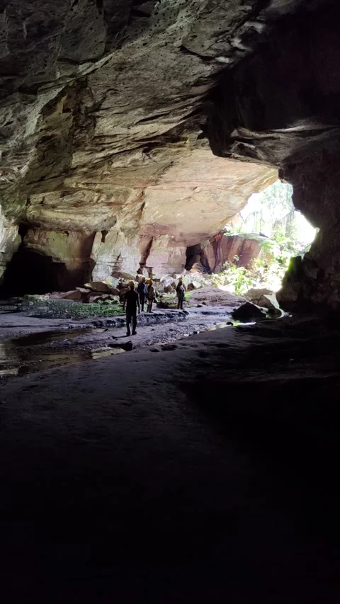 Explorers in cave in mossy terrain and sunlight illuminating rock formations Stock Footage 310142917