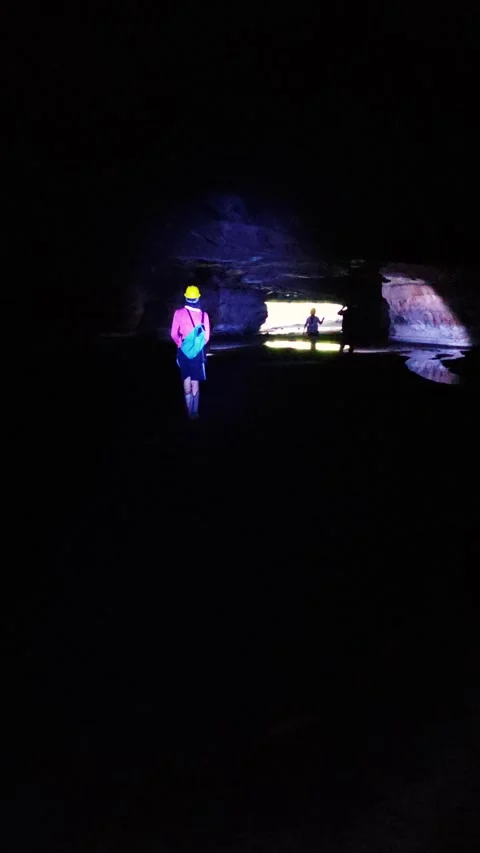 Explorers with headlamps walk dark cave tunnel toward lighted exit with helmets Stock Footage 310142910