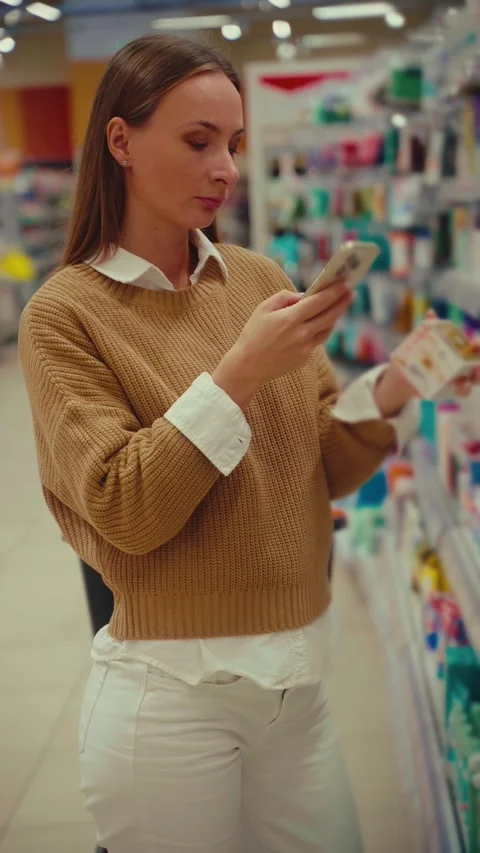 Exploring body cream options in a retail store while checking prices and 스톡 동영상 293675297