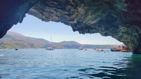 Exploring a Coastal Cave With Clear Water and Boats in the Bay During a Sunny Stock Footage 330794731