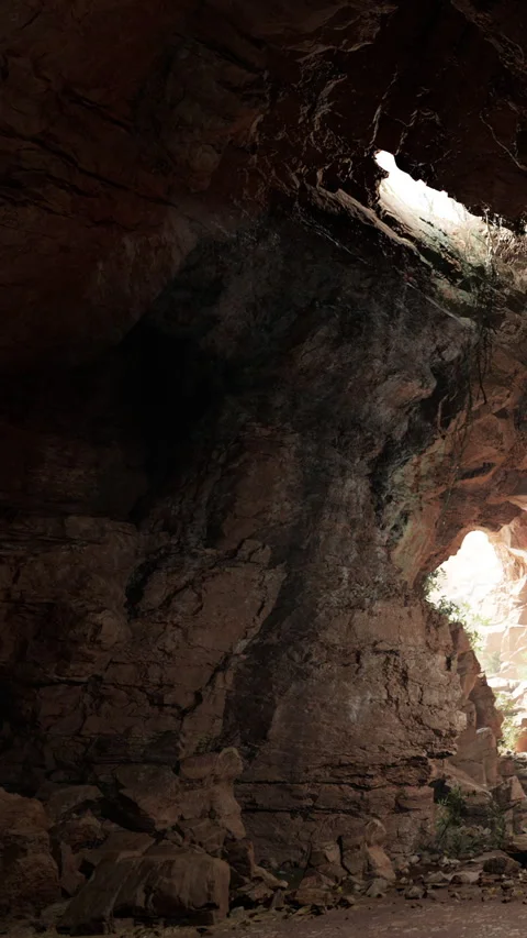 Exploring a dark cave with light shining through the entrance above Stock Footage 341249144