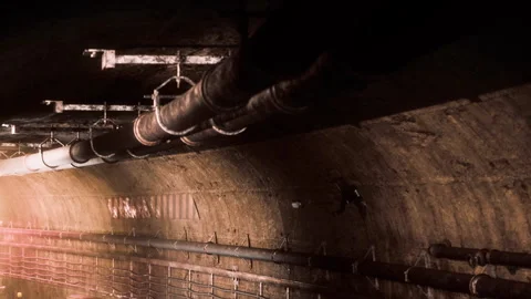 Exploring a dark underground tunnel with pipes above and rough walls Stock Footage 344964959