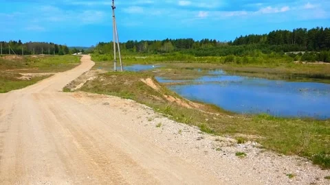 Exploring a dirt road by a pond surrounded by trees and fields on a sunny day in Vídeo Stock 327181495
