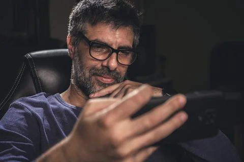 Exploring the Future. A man with glasses and dark hair immersed in his mobi.. Stock Photos
