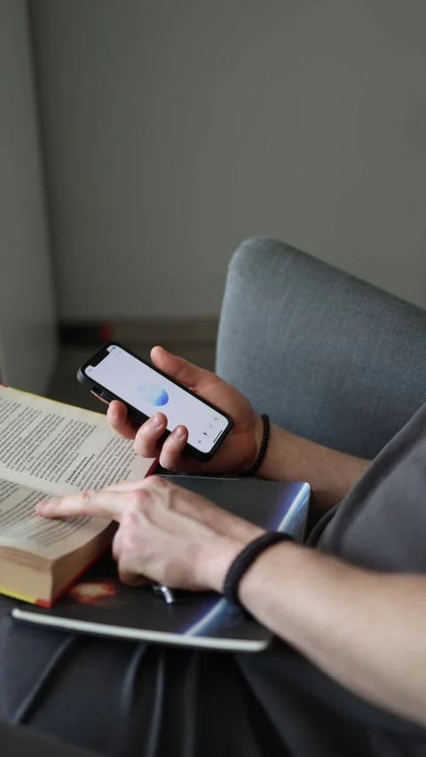 Exploring ideas with ChatGPT one hand turns the page the other holds the phone s Stock Footage 305999276