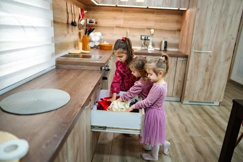 Exploring a kitchen drawer filled with colorful clothes by three young children Stock Photos