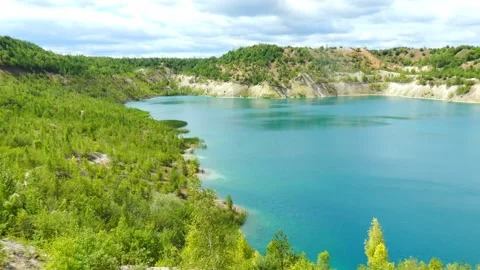 Exploring a lake surrounded by green hills in a quarry area on a cloudy day 動画素材 340448107
