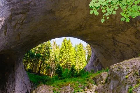 Exploring a natural stone arch surrounded by lush green forest during daytime Stock Photos