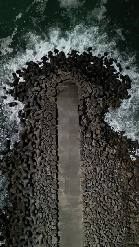 Exploring a rocky shoreline with crashing waves at a coastal pier during sunset Stock Footage 283766352