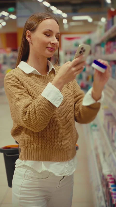 Exploring skincare options in a store while scanning face cream labels for Stock Footage 293674341