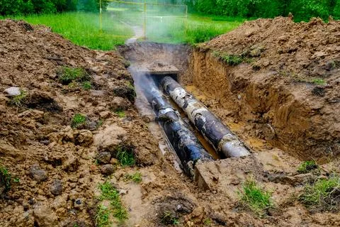 Exposed damaged heating pipelines in open trench with steam and muddy repai.. Stock Photos